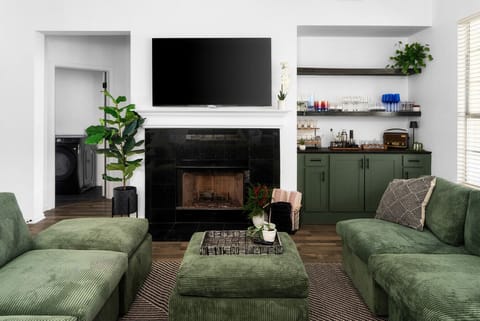 Cozy up in this stylish living room, featuring plush green seating, a warm fireplace, a built-in bar, and a large TV for the perfect blend of comfort and entertainment!