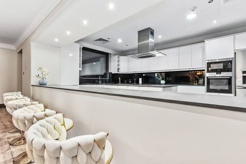 Sleek, modern kitchen with white cabinetry, black backsplash, and plush white bar stools.