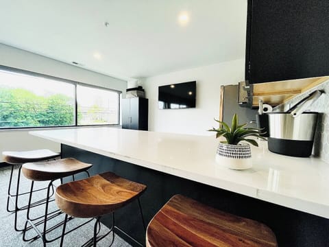 A sleek kitchen bar featuring stylish wooden stools and a mounted TV on the wall, creating a perfect spot to enjoy a meal or catch your favorite show while staying connected in the modern open-concept space.
