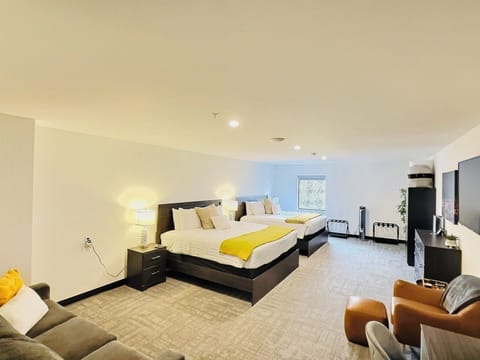 A bright, open room featuring queen beds, work desk, ample storage, and a large TV, perfect for relaxing or working during your stay.
