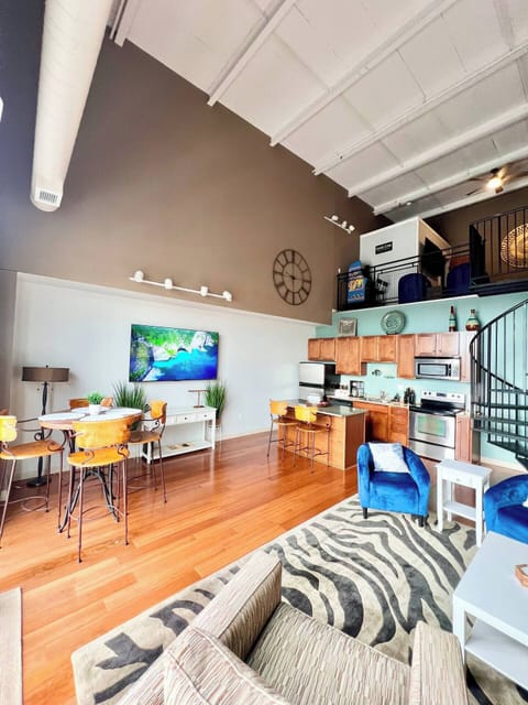 This airy open-concept space combines a modern kitchen and cozy living area. High ceilings and industrial-style beams create a spacious feel, while stylish furnishings and a zebra-print rug add character. Perfect for relaxing or entertaining guests!
