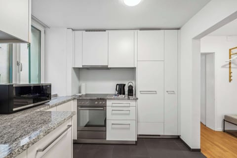 A clean and functional modern kitchen features sleek white cabinetry, stainless steel appliances, and a polished granite countertop.