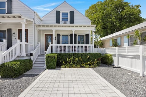 The charming exterior of the house, showing its white facade and a paved driveway. (1)