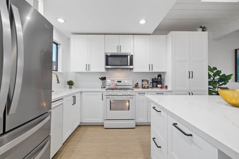 A well-appointed kitchen space featuring sleek white cabinetry and a marble countertop that extends throughout. The kitchen is equipped with modern stainless steel appliances, including a side-by-side refrigerator, oven, and microwave, all neatly integrat