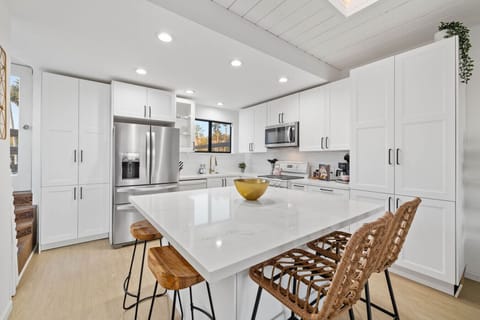 A sleek and contemporary kitchen with bright white cabinetry and stainless steel appliances, centered around a large marble island that serves as a focal point.