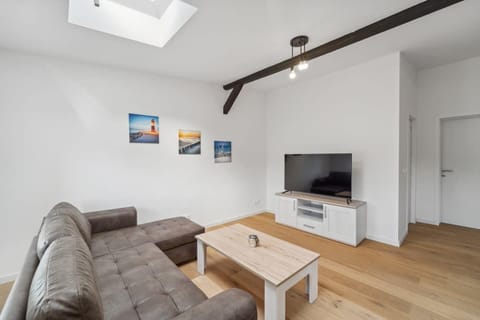 Das helle Wohnzimmer mit modernem Sofa, stilvollem Holztisch und großem Fernseher unter den Dachbalken lädt zum gemütlichen Verweilen ein.