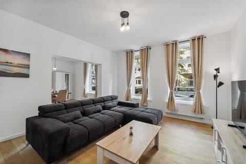 Großzügiges Wohnzimmer mit komfortablem Ecksofa, modernen Möbeln und viel Tageslicht durch die großen Fenster.