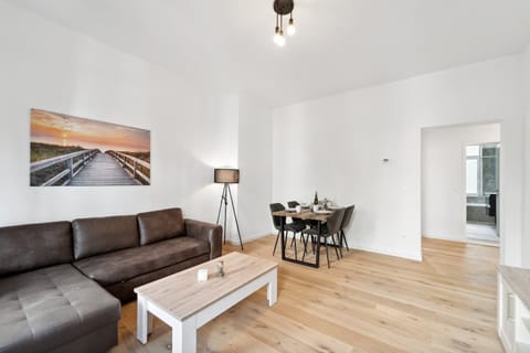 Das stilvolle Wohnzimmer in Wilhelmshaven bietet mit gemütlichem Sofa, modernem Essbereich und hellem Holzfußboden ein einladendes Ambiente für entspannte Abende.