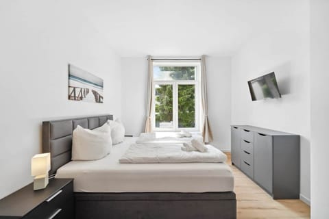 Das helle Schlafzimmer in Wilhelmshaven ist modern eingerichtet mit einem gemütlichen Doppelbett, großem Fenster, Wand-TV und stilvollem Stauraum für erholsame Nächte.