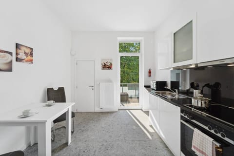 Die helle Küche in Wilhelmshaven ist mit moderner Ausstattung, weißem Hochglanz-Design und einem kleinen Essbereich eingerichtet und bietet Zugang zum Balkon.