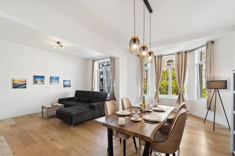 Das helle Wohn- und Esszimmer kombiniert eine moderne Essecke mit einem gemütlichen großen Sofa und ist durch die vielen Fenster lichtdurchflutet – ideal für entspannte Abende und gemeinsame Mahlzeiten.