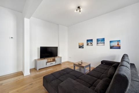 Das moderne Wohnzimmer überzeugt mit einem großen Sofa, Fernseher und geschmackvollen Wandbildern und lädt zu gemütlichen Filmabenden oder entspannten Stunden ein.