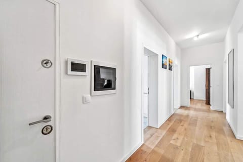 Der helle Flur mit Holzfußboden und weißen Wänden verbindet die verschiedenen Räume der Wohnung und ist mit modernen Wandbildern und klarer Linienführung freundlich gestaltet.