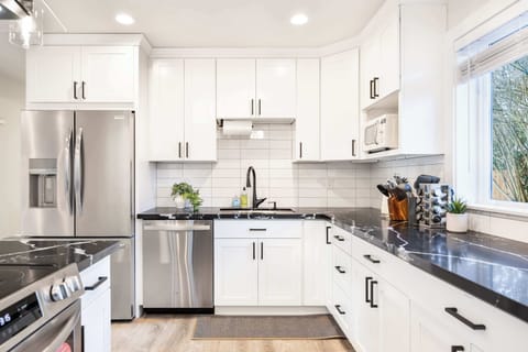 This fully modern kitchen is a chef’s dream come true. Featuring gleaming black marble-patterned countertops, pristine white cabinets, and top-of-the-line stainless steel appliances, it’s both functional and stylish.