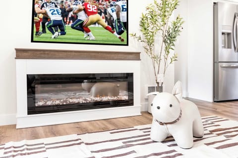 Gather around the sleek electric fireplace beneath a mounted flat-screen TV. The decorative elements, including a charming faux plant and a whimsical dog-shaped decor piece, add a playful yet sophisticated touch.