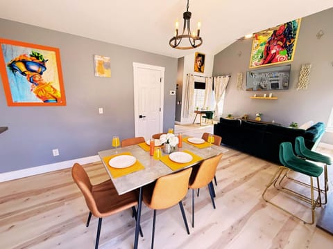 A stylish and inviting dining area with a modern table, sleek leather chairs, vibrant decor, and a chic chandelier—perfect for gatherings and memorable meals