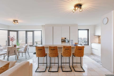 Modern open kitchen with ocean views. Features a sleek island, stylish barstools, and warm lighting, creating a bright and inviting space.
