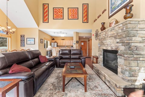 Spacious living area with vaulted ceilings, large windows providing ample sunlight, and electric reclining sofas surrounding the cozy fireplace.