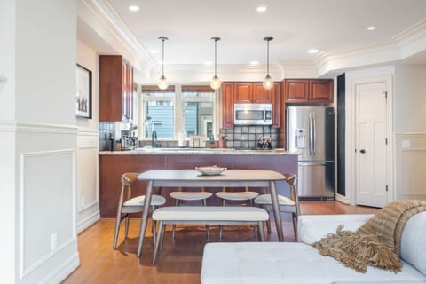 The dining table is a sleek wooden piece with a natural finish, surrounded by four matching chairs with beige upholstered seats and curved backrests