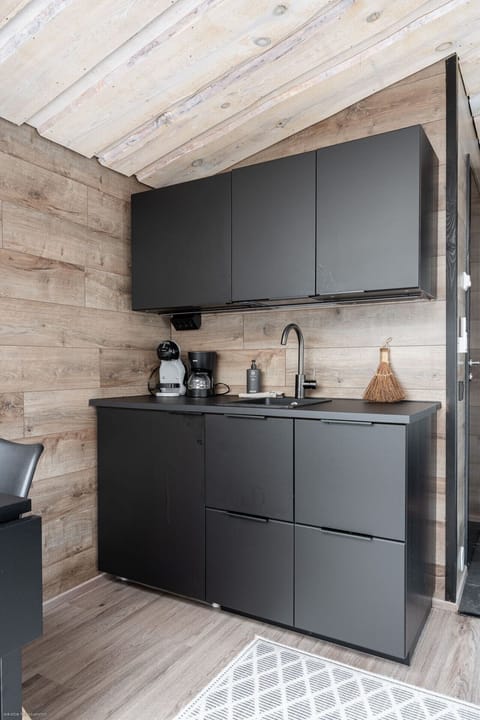 A modern, compact kitchenette provides everything you need for a comfortable stay, including a coffee maker and a Nespresso machine. The sleek, black design beautifully complements the warm wood paneling, offering a stylish and convenient space for prepar