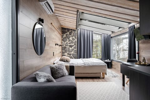 This modern studio offers a cozy and inviting space, complete with a comfortable bed and stylish sofa. The unique interior blends warm wood and a rustic stone wall, while the expansive glass wall immerses you in the beautiful surrounding landscape from th