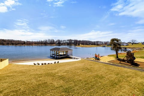 Expansive Backyard: Beautifully manicured lawn gently slopes down to a private sandy beach, dock, and play area, all framed by stunning panoramic views of Lake Anna.