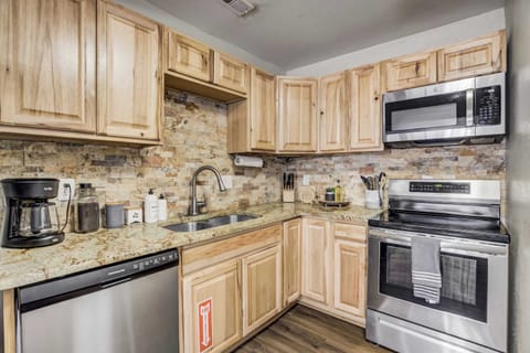 The fully-equipped kitchen features rustic wood cabinetry, stainless steel appliances, and a stylish stone backsplash. Stocked with cookware, utensils, and a coffee maker, this space is perfect for preparing home-cooked meals or quick snacks.