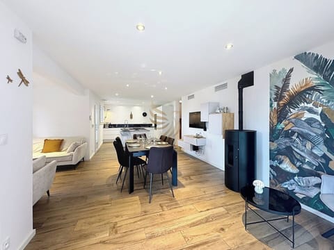 Un espace idéal pour des repas conviviaux, la pièce à vivre propose un poêle chaleureux. Savourez un moment de détente sur le canapé face au mural végétal inspirant.