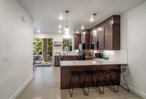 Fully equipped kitchen featuring sleek stainless steel appliances, pendant lighting, and a large island with barstool seating for four.