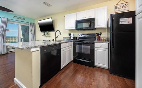 This kitchen features sleek black appliances, granite countertops, and a beach view, perfect for enjoying meals together