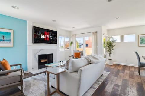 Sun-soaked living room with open dining area and amazing ocean-view patio—perfect for soaking in the beach weather. Features a wood-burning fireplace and a 65-inch television.
