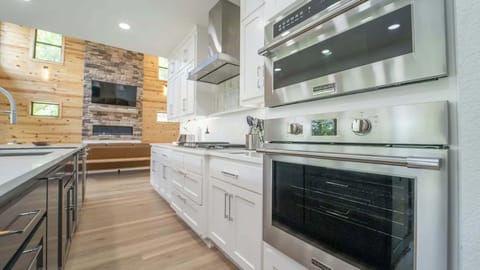 Sleek modern kitchen with stainless steel Frigidaire appliances, bright white cabinetry, and a cozy open layout leading into a wood-accented living area with a stone fireplace.