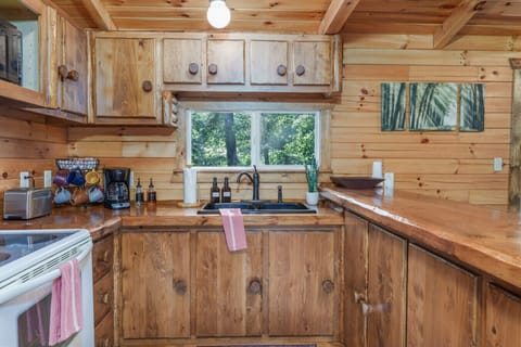 Rustic kitchen with wooden cabinets, large countertop, and window view of lush greenery—perfect for preparing meals in cozy cabin style 🍳🌲🍽️