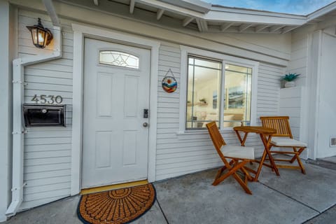 A beautiful front patio with a bistro-style seating area, perfect for enjoying your morning coffee or evening wine. The white exterior, warm lighting, and inviting atmosphere create the perfect getaway.
