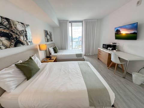 Spacious bedroom with a two beds, flat-screen TV, and bright natural lighting.