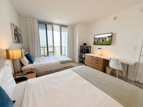 Spacious bedroom with a two beds, flat-screen TV, and bright natural lighting.