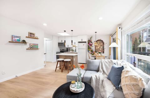 A modern and bright living area featuring a comfortable seating arrangement, sleek kitchen with island seating, and a colorful floral area