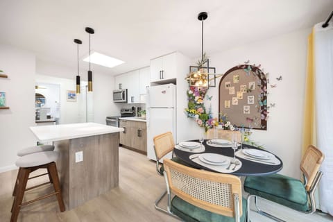 Dine in style in this modern, well-lit space featuring chic urban décor with a striking Floral centerpiece, sleek kitchen, and a view into the airy outdoor area.