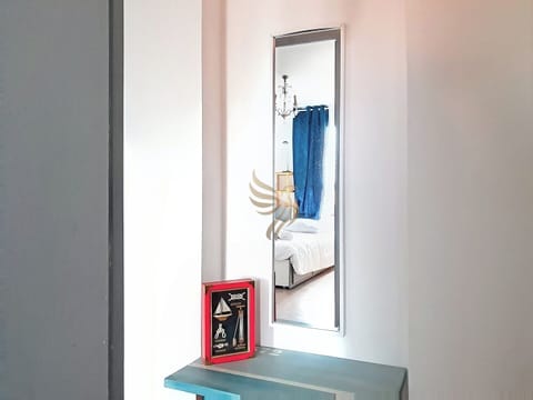 Un couloir avec un miroir reflétant une chambre, bleu et blanc, minimaliste, une table avec une boîte rouge.