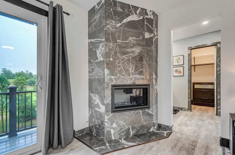 Elegant double-sided fireplace in the primary suite with access to the balcony and walk-in closet beyond.
