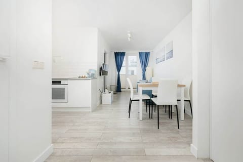 A spacious living and dining area with a light wood table, white chairs, and a blue sofa in the background.