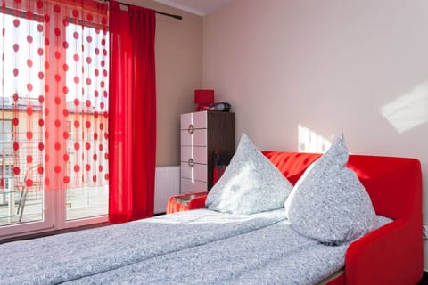 Large windows with sheer red curtains fill the room with natural light, creating a welcoming atmosphere.
