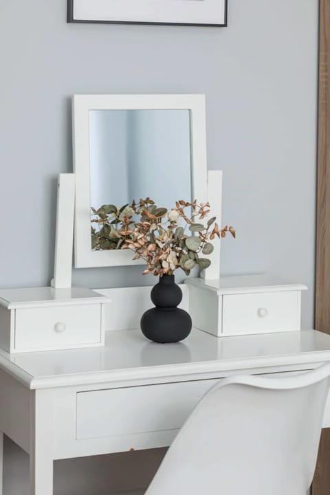 A white dressing table with a mirror and a decorative flower arrangement. Adds a touch of elegance and functionality to the space.