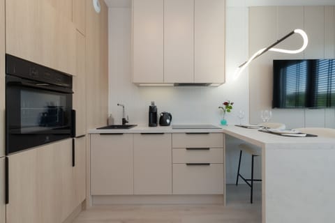 A modern kitchenette with white cabinets, and full appliances like kettle, oven, stove,  offers cooking convenience and interior elegance.