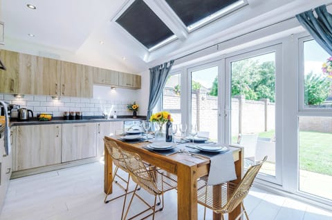 Bright, modern kitchen with full appliances, stylish wood cabinetry, and a spacious dining area. Enjoy meals at the rustic table with views of the garden through large French doors. Perfect for cooking, dining, and gathering.