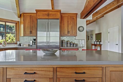 Modern kitchen detail focusing on a large island and a stainless steel refrigerator flanked by warm wooden cabinetry and a subway tile backsplash.