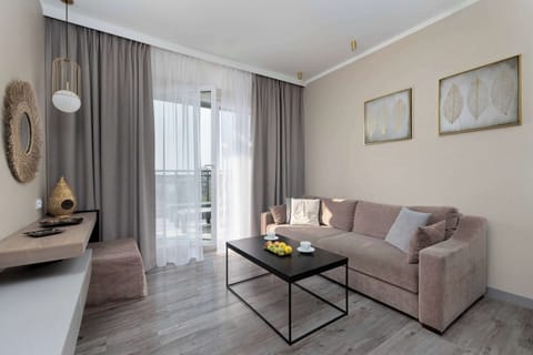 A cozy living room space with a sofa, coffee table, and TV. The large window brings in natural light, creating a warm and inviting atmosphere.