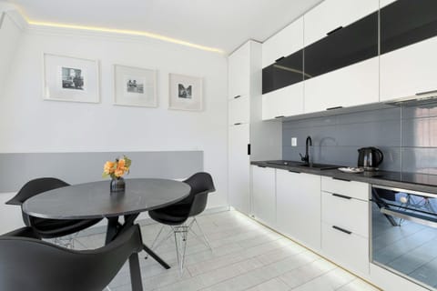 A well-lit kitchen area featuring white cabinetry, modern appliances, and a dining table with fresh flowers.


