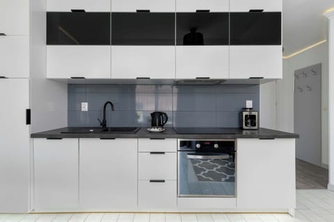 Fully equipped kitchenette with sleek white cabinetry and black backsplash.