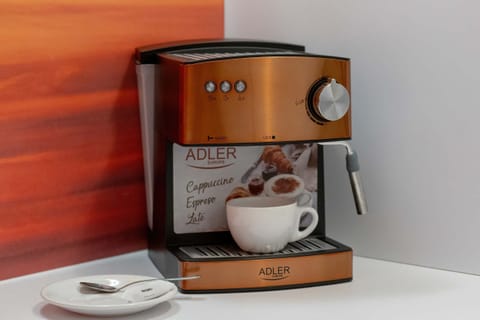 A sleek coffee station with a high-end coffee machine, a cup, and decorative details set against a bold orange backsplash.

